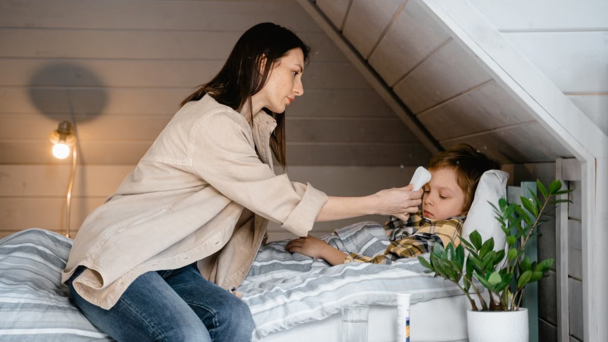 A mother checks her sick child's temperature in a cozy bedroom setting, showcasing care and parenting.